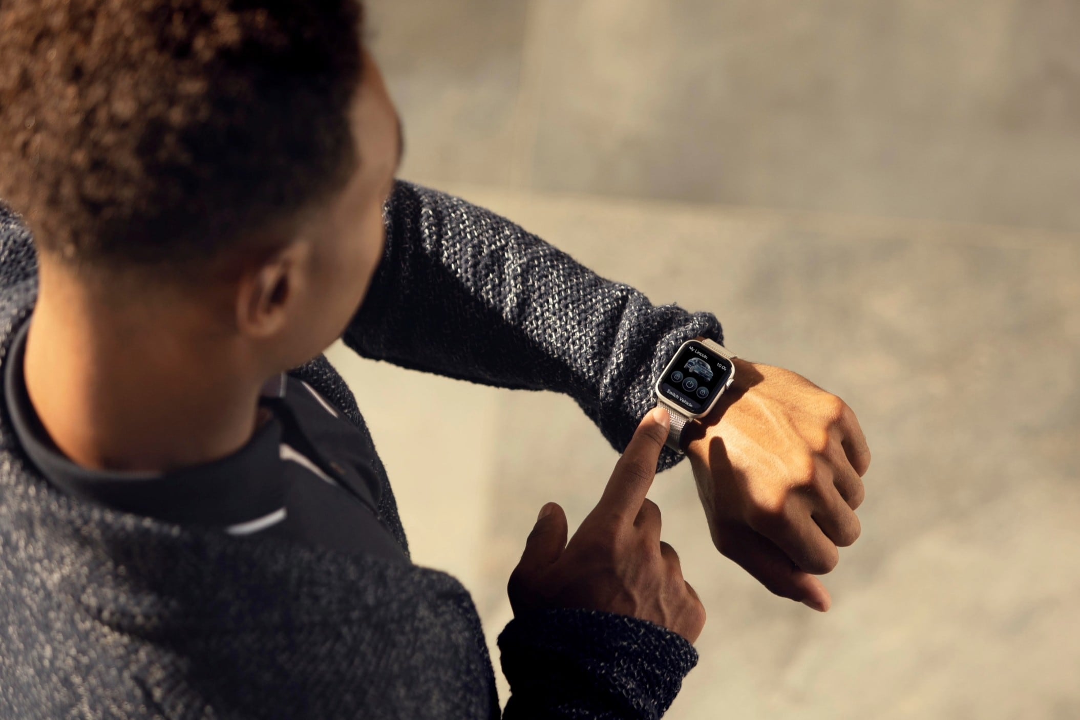 Person interacting with a smartwatch, wearing a gray jacket, in a bright setting.