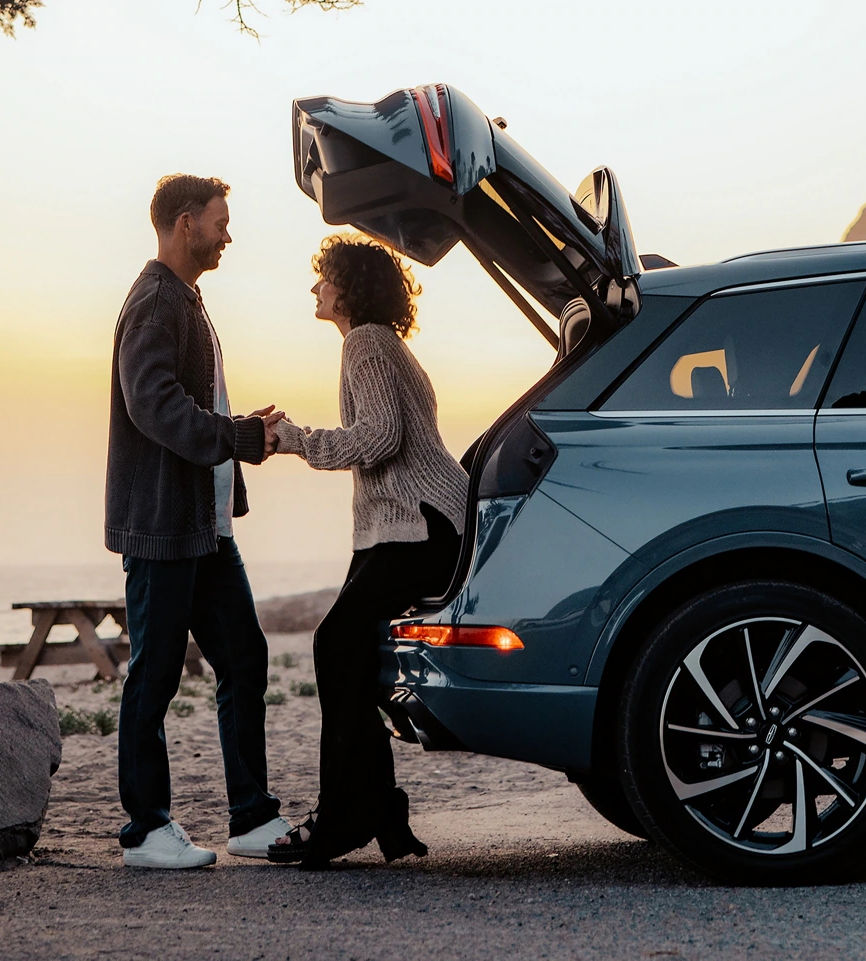 Couple enjoys sunset at beach beside an SUV, enhancing travel experience and connection.